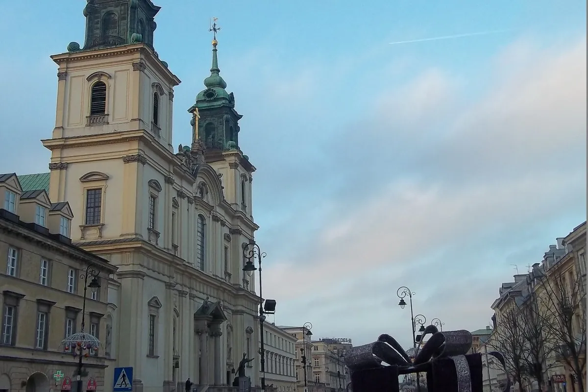 Die cremefarbene Doppelturmfassade der Heilig-Kreuz-Kirche, gesehen von einer Warschauer Straße in der Abenddämmerung mit grünem Kupferdach